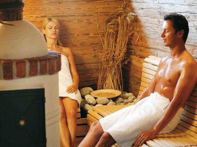Twee personen zittend in een houten saunaruimte, beiden gewikkeld in handdoeken.