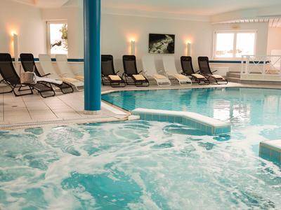 Binnenruimte met bubbelbad en zwembad, meerdere ligstoelen bij het zwembad.