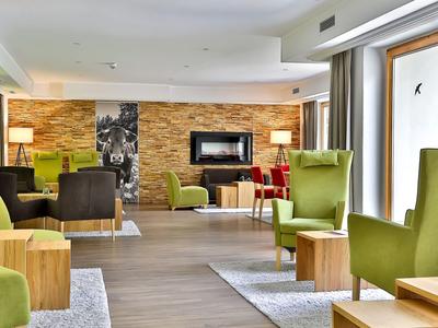 Gemütlicher Lounge-Bereich mit grünen Sesseln, Holztischen und Steinwand im modernen Stil.