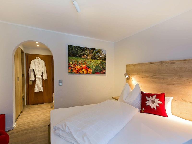 Helder verlichte hotelkamer met twee bedden, rode kussens en een badjas op de achtergrond