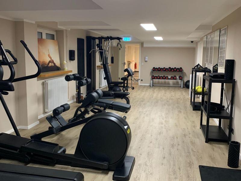 Kleine hotelgym met loopband, fitnessapparatuur en halters op lichte houten vloer.