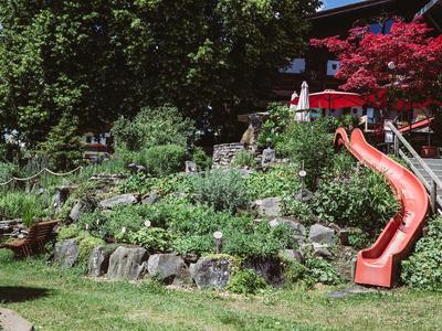 Tuin met terrassentuin, groene planten en een rode glijbaan naast een trap.