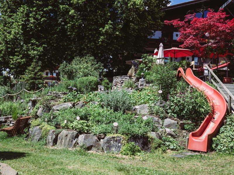 Tuin met terrassentuin, groene planten en een rode glijbaan naast een trap.