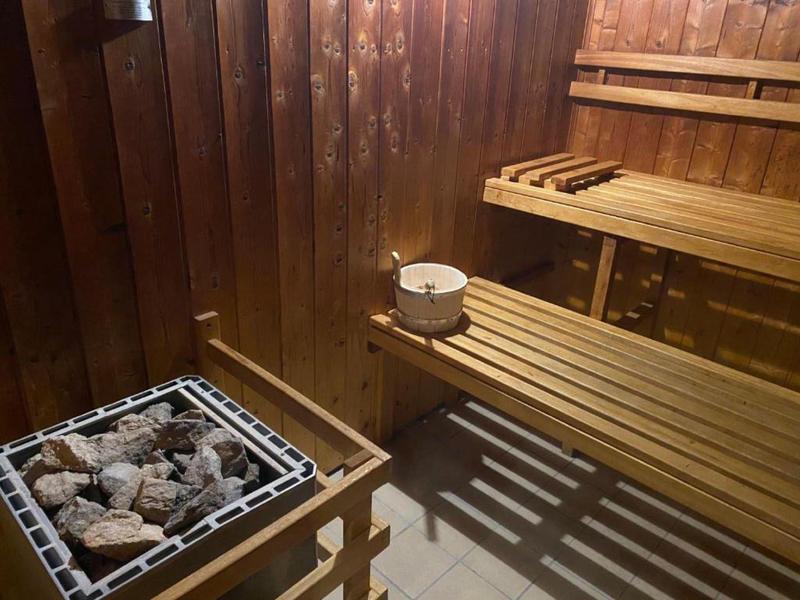 Wooden sauna with sauna stones, wooden benches, and a pouring bucket on the bench.