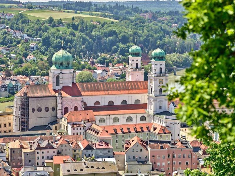 A large historic church with four green domes, surrounded by town and trees.