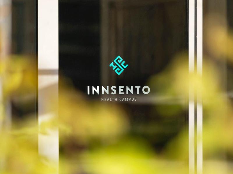 Glass door with Innsento Health Complex logo and blurred plants in the foreground.