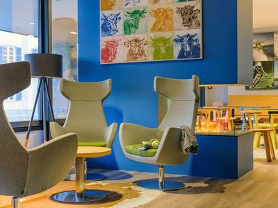 Modernes Wartezimmer mit grauen Sesseln, blauem Akzentwand und buntem Kunstwerk.