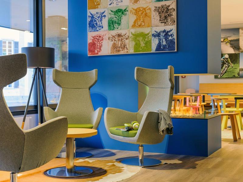 Area lounge moderna con poltrone eleganti, pavimento in legno e arte murale colorata.