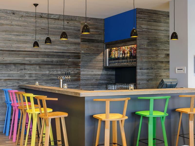 Bar moderno con sgabelli colorati in legno e lampade a sospensione in un ambiente elegante.