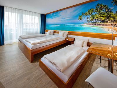 Camera d'hotel luminosa con due letti e grande murale a parete di una spiaggia.