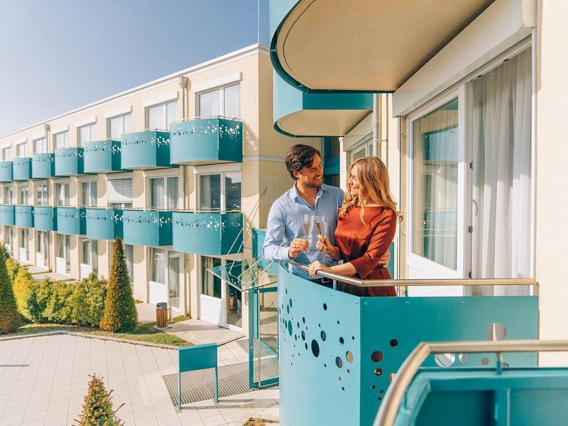 Coppia su balcone di un hotel moderno con ringhiere turchesi e cielo sereno.