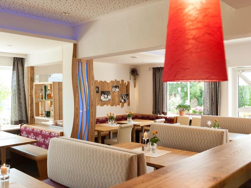 Salle à manger moderne et chaleureuse avec meubles en bois clair et grands abat-jours rouges.