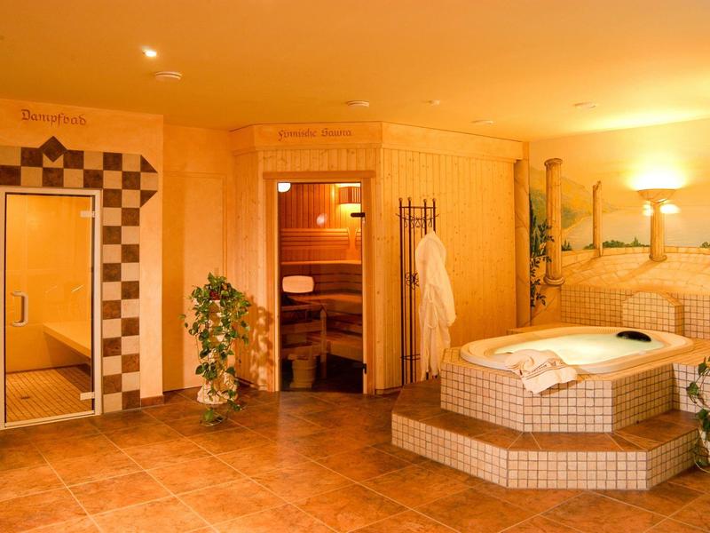 Salle de spa lumineuse avec jacuzzi, sauna, douche et éclairage relaxant.