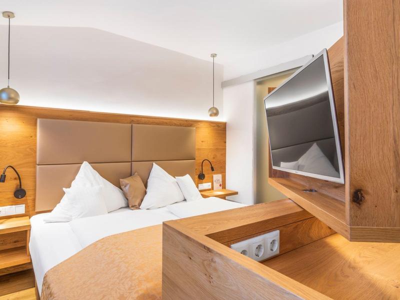 Camera d'hotel moderna con letto matrimoniale, rivestimento in legno e TV a schermo piatto a parete.