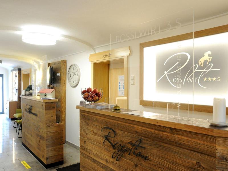 Area reception dell'hotel luminosa con scrivanie in legno, logo e dettagli decorativi.