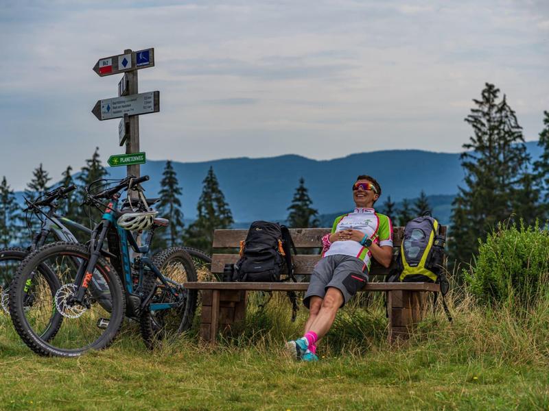 Persona che si rilassa su una panchina con biciclette e cartelli in un paesaggio montano