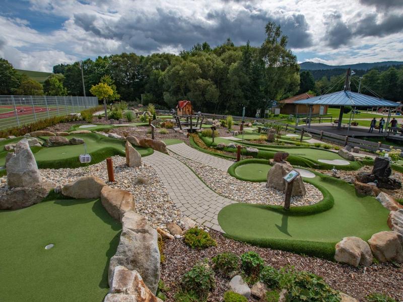 Campo da mini golf all'aperto con più buche, superfici di gioco verdi e natura circostante.