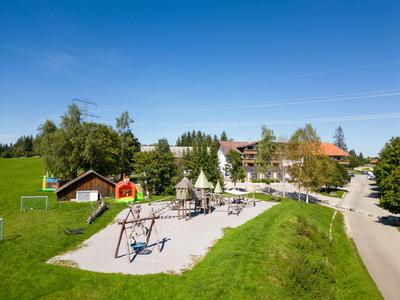 Playground with swings and slide in front of hotel buildings in green landscape under blue sky