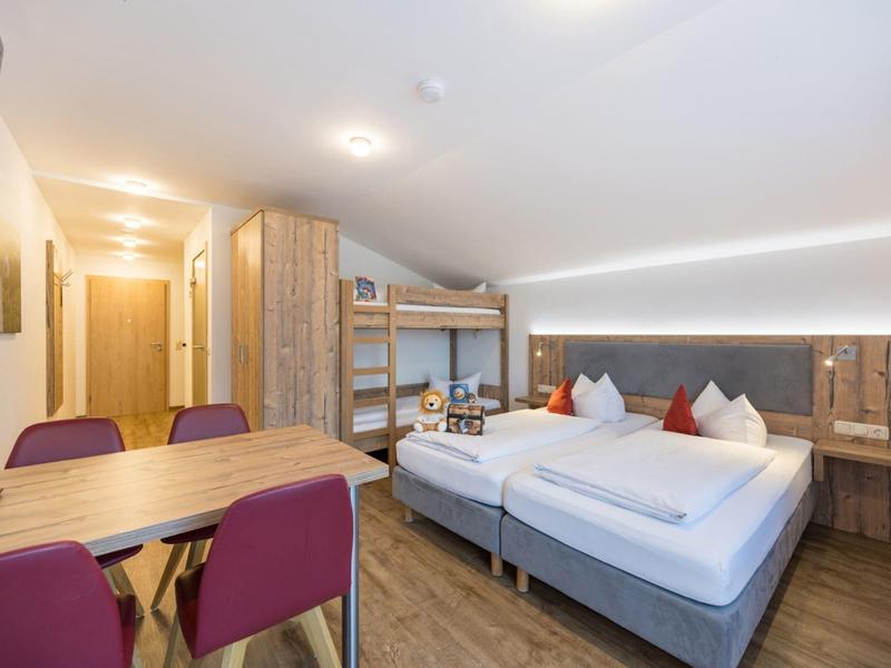 Chambre d'hôtel moderne avec lit double, lits superposés et table à manger avec chaises.