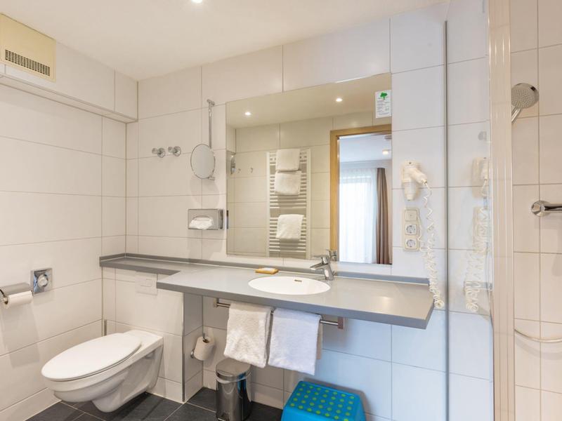 Salle de bain lumineuse avec toilettes, lavabo, grand miroir et douche dans une chambre d'hôtel.