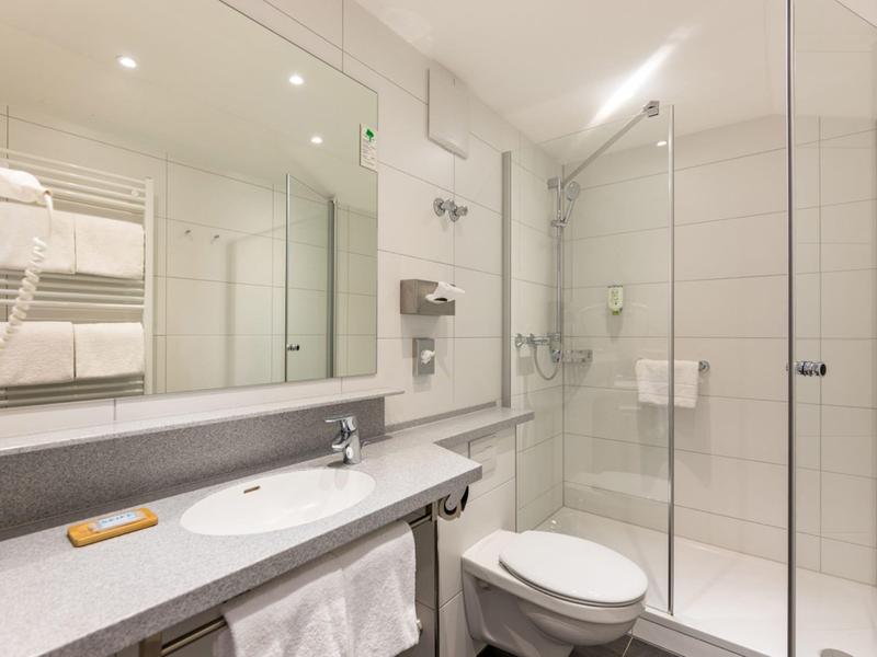 Salle de bain propre et moderne avec douche en verre, grand miroir et carrelage blanc.