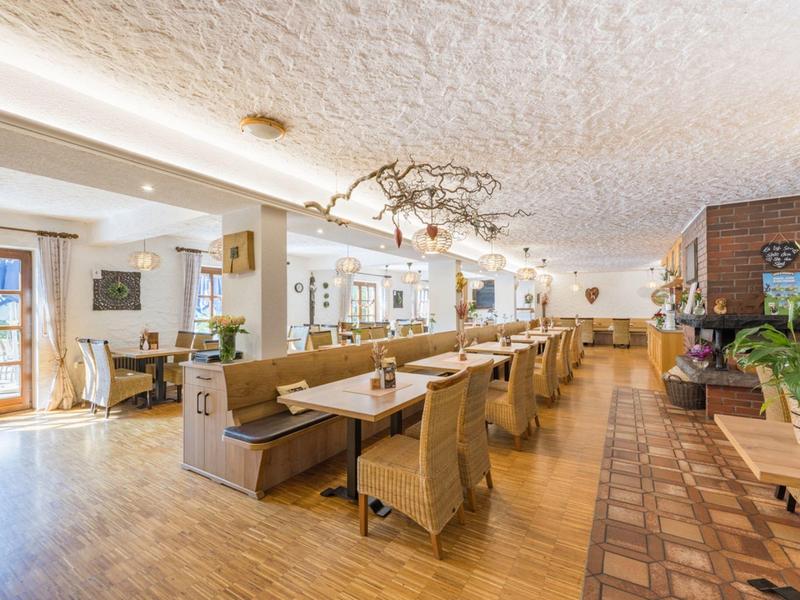Restaurant lumineux avec mobilier en bois, grandes fenêtres et plafond rustique.