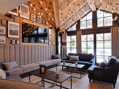 Przytulna część wypoczynkowa z sofami, stolikami i dużymi oknami w ciepłym, drewnianym wnętrzu.