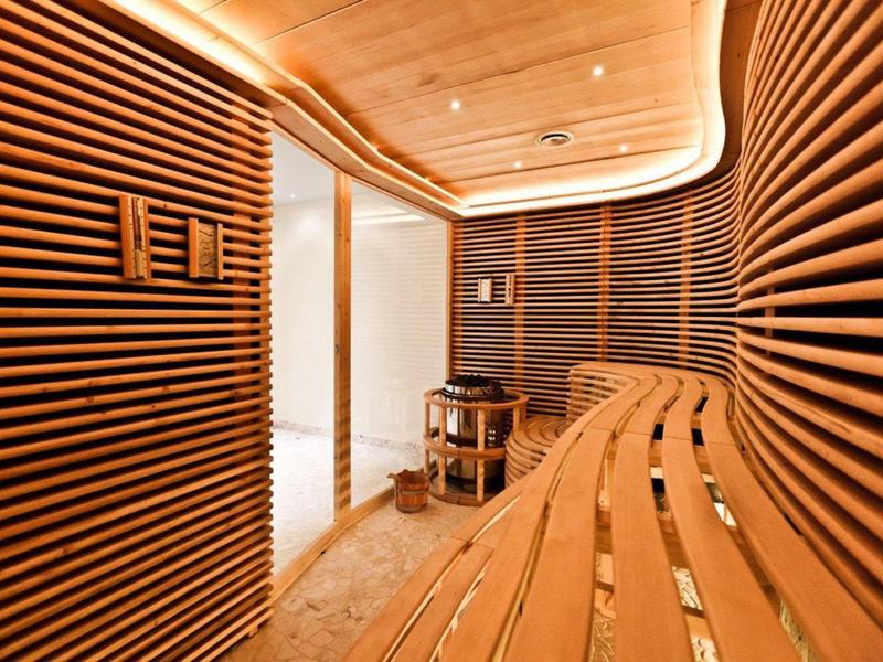 Moderne Sauna mit geschwungenen Holzbänken und Wandpaneelen, warmes Licht, heller Boden.