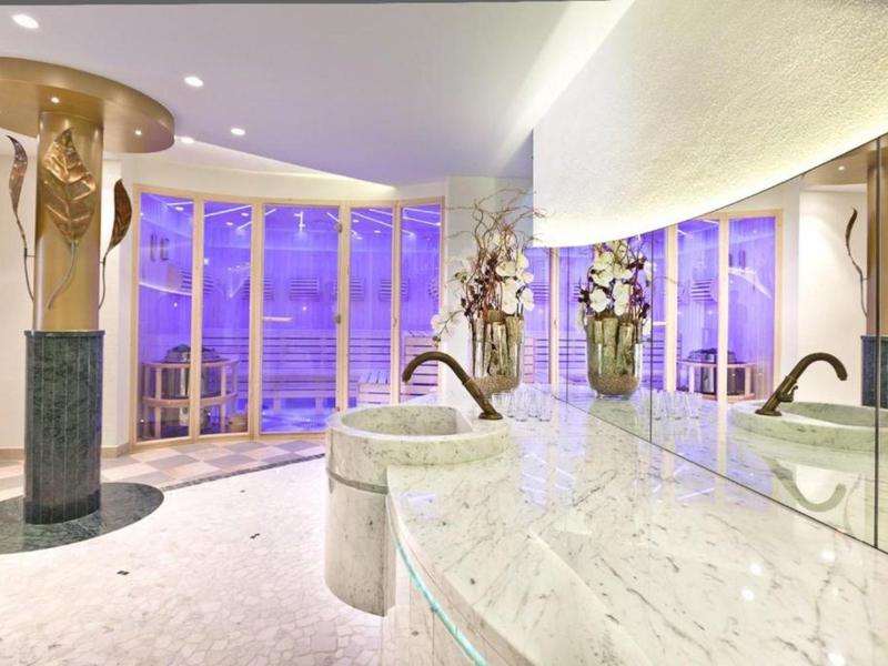 Luxuriöses Spa mit Marmorwaschbecken und großen Fenstern mit Blick aufs Meer bei Dämmerung.