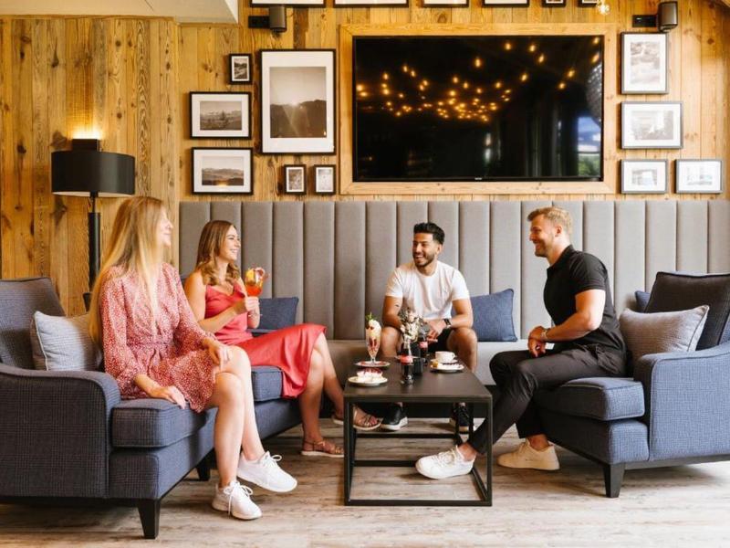 Vier Personen unterhalten sich gemütlich in einer modernen Hotel-Lounge mit Holzwänden.