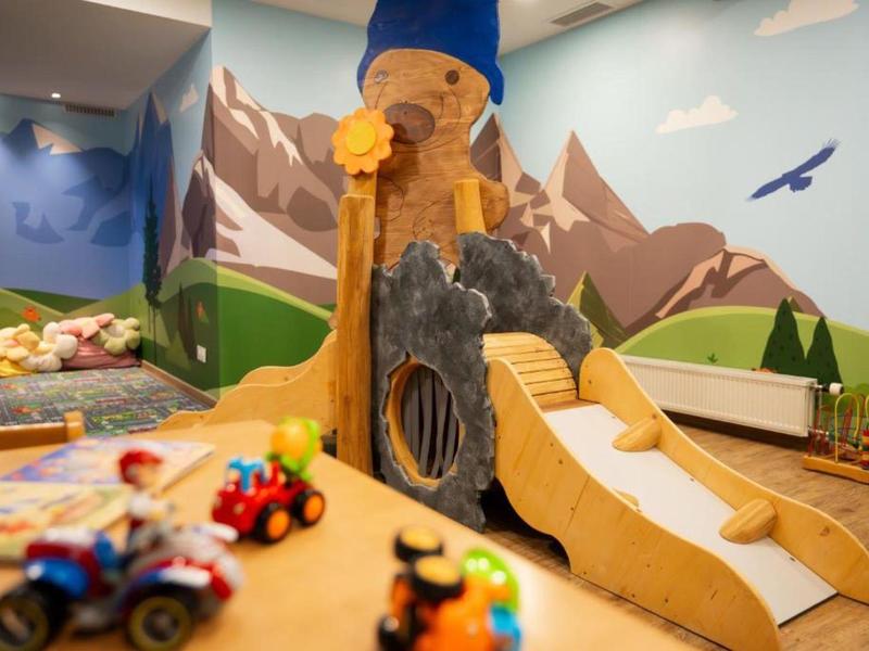 Bunter Indoor-Spielbereich mit Rutsche und Bergmotiven an der Wand.
