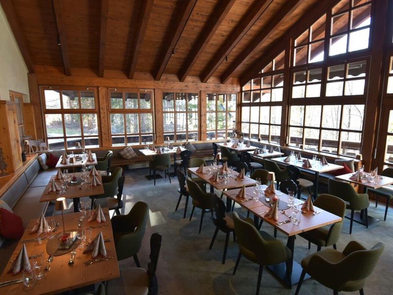 Licht ingericht restaurant met houten balkenplafond en grote ramen voor daglicht.