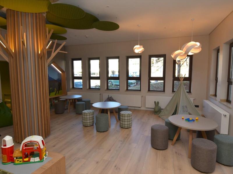 Lichte speelruimte met houten boomstammen, zitplaatsen en speelgoed in een kamer met grote ramen.