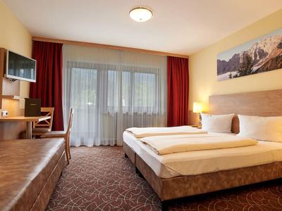 Gezellige hotelkamer met tweepersoonsbed, bureau, tv en groot raam met gordijnen.