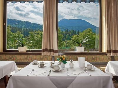 Een gedekte ontbijttafel bij grote ramen met uitzicht op bergen en planten.