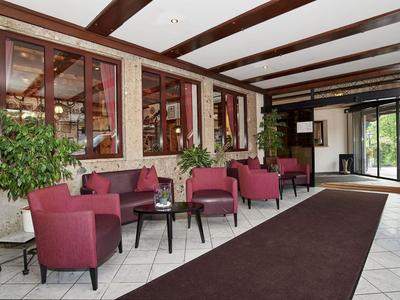 Lichte hotellobby met rode fauteuils, planten en toegang tot een balkon.