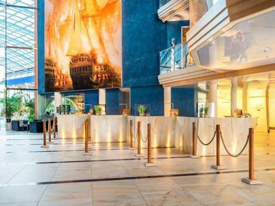 Luxusní hotelová hala s mramorovou podlahou, zábranami a velkým uměleckým dílem na zdi