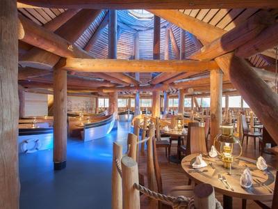 Rustikální restaurace s dřevěnými trámy, kulatými stoly a útulným osvětlením.