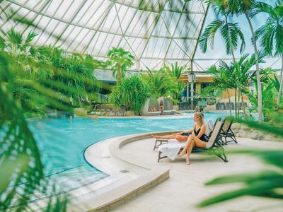Žena relaxuje na lehátku vedle tropického vnitřního bazénu s rostlinami pod skleněnou kupolí.