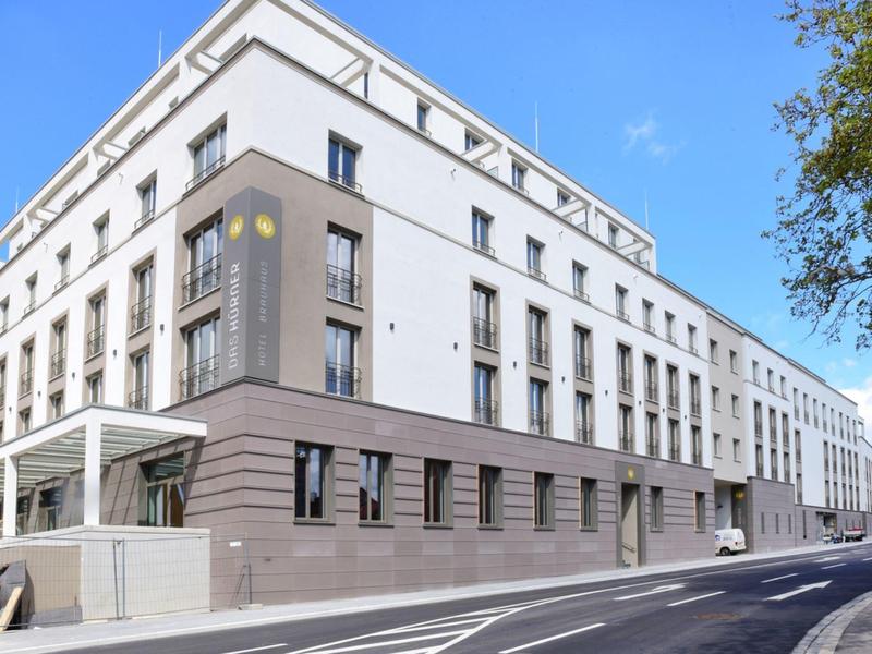 Modernes Hotelgebäude mit weißer Fassade und großen Fenstern an einer Straßenecke.