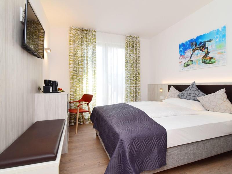 Helles Hotelzimmer mit großem Bett, Fernseher, Sitzbereich und moderner Dekoration.