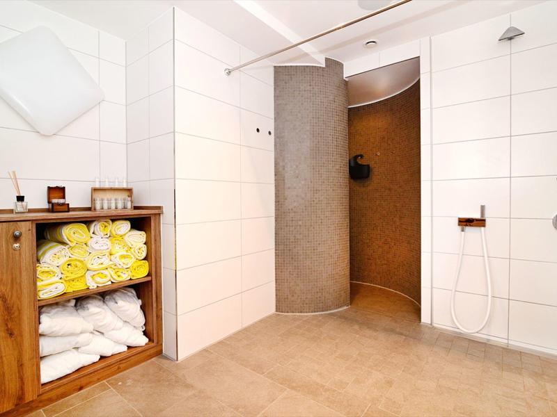 Moderne Dusche mit offenem Eingang, weißen Wänden und Holzregal mit gelben Handtüchern.