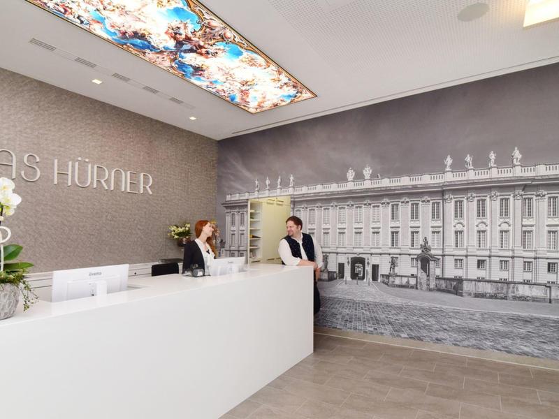 Moderne Hotellobby mit weißem Empfangstresen und Wandbild eines historischen Gebäudes.