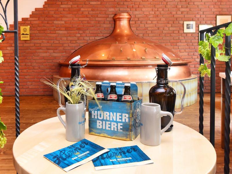 Rundes Holztisch mit Bierflaschen, Gläsern und Boutique vor Kupferbrauerei in rustikalem Interieur.