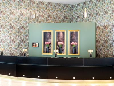 Modern balie voor een groene muur met bloemenbehang en drie afbeeldingen van bloemstukken.