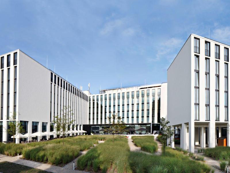 Modern hotelgebouw met grote glazen gevel en goed onderhouden tuin op de voorgrond.