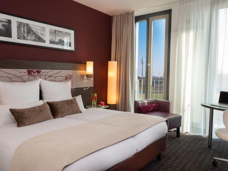 Moderne hotelkamer met groot bed, bureau en ramen van vloer tot plafond.