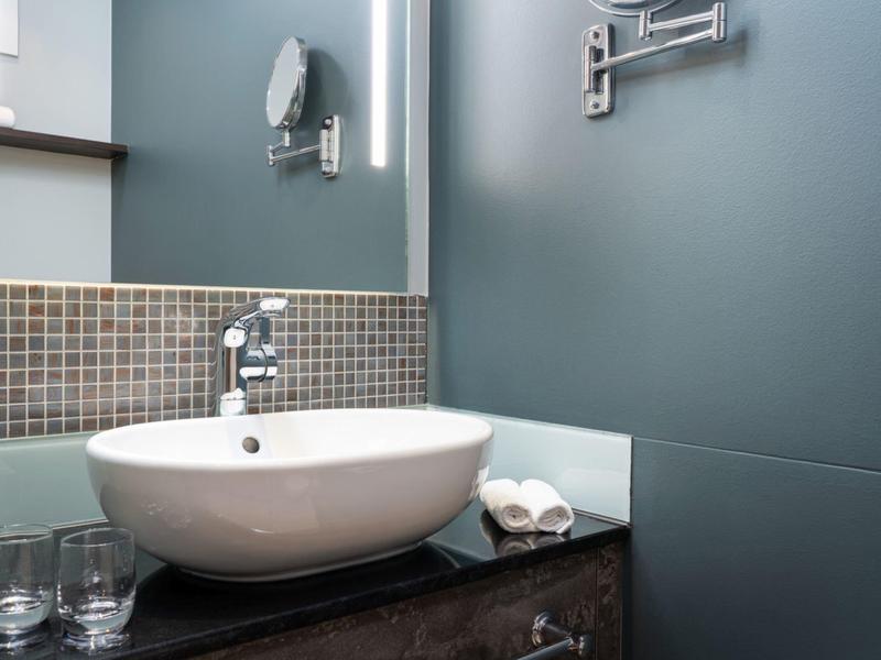 Moderne badkamer met ronde wastafel op donkere aanrecht en grijze muur.