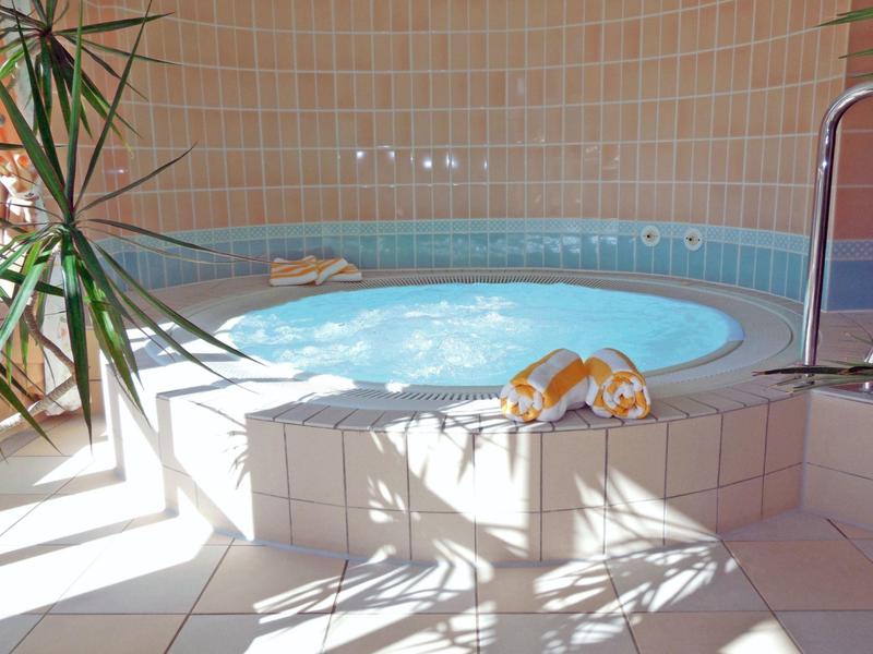 Piscine intérieure chauffée avec effet bulles, serviettes sur les marches et plante au premier plan.