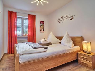 Camera da letto luminosa con letto matrimoniale, tende rosse e mobili in legno.